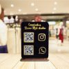 Black and gold acrylic qr code stand on a shop counter displaying GPay and Instagram scanner codes.